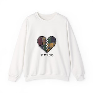 Puede incluir: Sudadera blanca con un diseño de corazón dividido hecho de tela de retazos en tonos rojos, verdes, amarillos y azules. El texto "STAY LOUD" está impreso debajo. Una parte superior informal y cómoda.