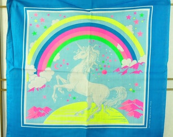 May include: A blue bandana with a white unicorn standing on a yellow crescent moon. The unicorn is surrounded by a rainbow with pink, green, and yellow stripes. There are stars and clouds in the background.