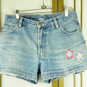 May include: Light blue denim shorts with frayed edges and embroidered flowers in pink, white, and green.