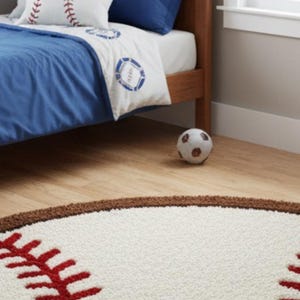 Puede incluir: Una alfombra circular con una superficie blanca texturizada, patrones de costuras de b&eacute;isbol en rojo y un borde marr&oacute;n. La alfombra est&aacute; dise&ntilde;ada para parecerse a una pelota de b&eacute;isbol, sirviendo como revestimiento tem&aacute;tico para el suelo.