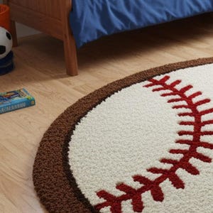 Puede incluir: Una alfombra redonda y texturizada dise&ntilde;ada con la apariencia de una pelota de b&eacute;isbol, con un centro color crema, un borde marr&oacute;n oscuro y detalles de costuras rojas. La alfombra tiene una construcci&oacute;n de pelo grueso sobre suelo de madera.