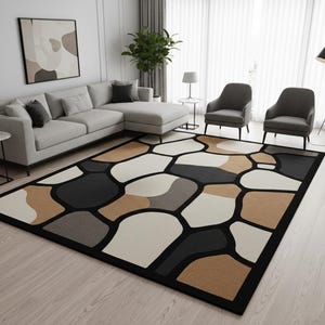 Puede incluir: Una alfombra rectangular con un diseño de guijarros en tonos negros, beige, grises y crema. La alfombra tiene un borde negro y está colocada sobre un suelo de madera clara. La alfombra está en un salón con un sofá seccional gris y dos sillones grises.