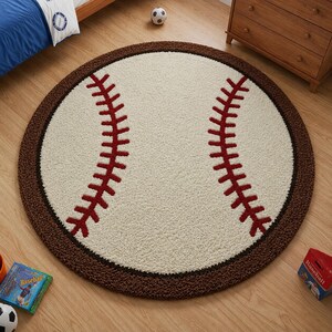 Puede incluir: Una alfombra circular con dise&ntilde;o de pelota de b&eacute;isbol, que presenta un centro color crema, dos patrones de costuras rojas curvas y un borde texturizado de color marr&oacute;n oscuro. La alfombra tiene una construcci&oacute;n de pelo copetudo.