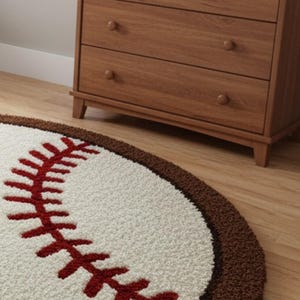 Puede incluir: Una alfombra redonda con dise&ntilde;o de b&eacute;isbol, centro color crema, costuras rojas y un borde marr&oacute;n grueso. La alfombra tiene una superficie texturizada de pelo largo y est&aacute; colocada sobre un suelo de madera clara en una habitaci&oacute;n.