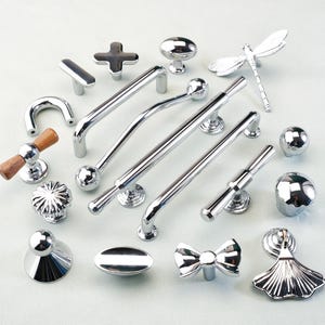 May include: A collection of chrome cabinet hardware, including knobs, pulls, and decorative accents. Designs include a dragonfly, bow, and various geometric shapes. The hardware is displayed on a light background.