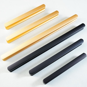 May include: A selection of gold and black cabinet pulls. The gold pulls have a brushed finish, while the black pulls have a matte finish. The pulls are rectangular with rounded ends, and vary in length.