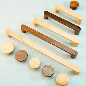 May include: An assortment of wooden cabinet hardware, including several pull handles and round knobs. The pulls vary in length and color, with some being light-colored and others a darker brown. The knobs are also in varying shades of wood.