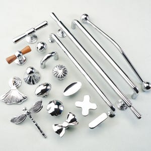 May include: An assortment of polished chrome cabinet hardware, including handles, knobs, and pulls. Designs include a dragonfly, bow, and various geometric shapes. Some pieces have wooden accents.