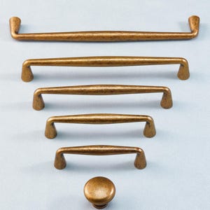 May include: A collection of bronze-colored cabinet hardware, including several sizes of bar pulls and a round knob. The hardware has a hammered texture and a warm, antique finish, suitable for kitchen or bathroom cabinetry.