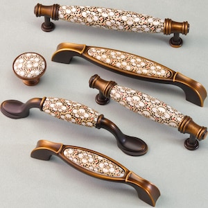May include: A collection of cabinet hardware, including handles and a knob. The hardware features a bronze finish and a ceramic center with a white floral pattern and brown accents. The set includes various handle sizes.