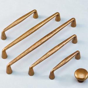 Può includere: Set di cinque elementi hardware per mobili color bronzo. Include quattro maniglie di diverse lunghezze e un pomello rotondo. L'hardware ha una texture martellata e una finitura metallica calda.