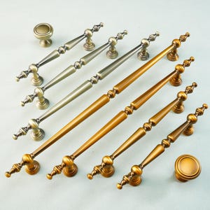 Puede incluir: Un surtido de herrajes para armarios de estilo antiguo, que incluyen pomos y tiradores. Los herrajes presentan varios acabados metálicos, como oro y plata. Las manijas varían en longitud, la más larga mide aproximadamente 30 cm.