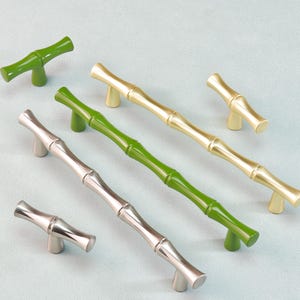 May include: A collection of bamboo-style cabinet pulls in various colors. The pulls are in green, silver, and gold, with a bamboo stalk design. The hardware is shown on a light blue background.