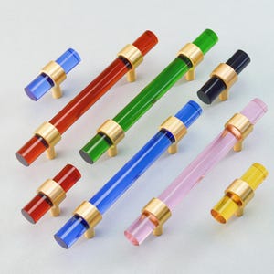 May include: A collection of colorful cabinet pulls in various sizes. The pulls feature clear acrylic rods in red, green, blue, black, pink, and yellow, accented with gold-toned metal hardware. These decorative pulls are designed for furniture.