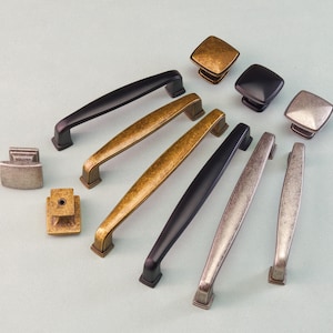 May include: A collection of cabinet hardware, including handles and knobs, in various finishes. The selection features black, antique brass, and silver-toned metal pieces. The handles are approximately 5 to 8 inches long.