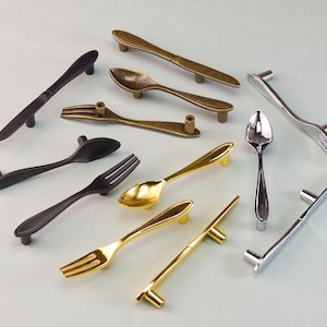 Könnte beinhalten: Eine Sammlung von Schrankgriffen in Form von Besteck. Die Griffe sind in verschiedenen Metallausführungen wie Gold, Silber und Bronze erhältlich. Das Set umfasst Designs von Löffeln, Gabeln und Messern für einen einzigartigen Akzent.