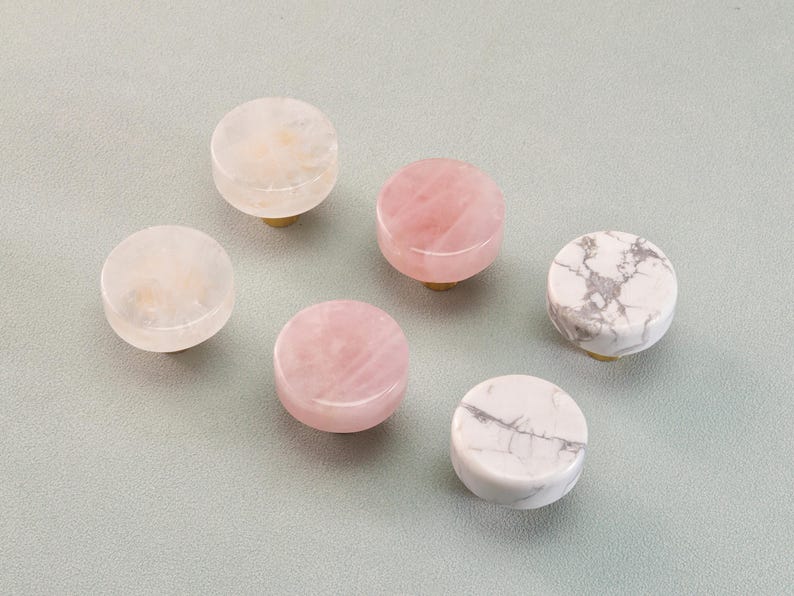 May include: Six decorative cabinet knobs in various colors and patterns. The knobs are round with brass stems. Colors include white, pink, and white with gray veining. These knobs are made of natural stone.