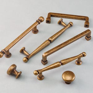 May include: Collection of antique brass cabinet hardware, including various sizes of handles and knobs. The hardware features a warm, aged finish and decorative detailing, suitable for kitchen or furniture projects.