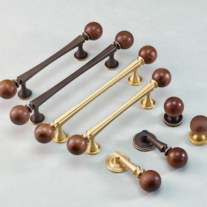 May include: A collection of cabinet hardware, including bronze and brass handles with wooden ball knobs. The handles vary in length and design, with some having a straight bar and others a curved shape. Several matching knobs are also included.
