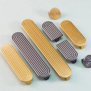 Peut inclure: Ensemble de poignées et de boutons de meubles dorés et argentés. Le matériel présente un design rainuré et arqué. Les poignées sont rectangulaires et les boutons sont circulaires. Sur fond bleu clair.