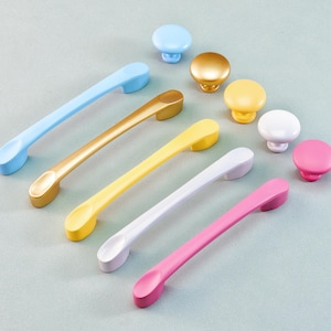 Pode incluir: Uma coleção de ferragens coloridas para armários, incluindo puxadores azuis claros, dourados, amarelos, brancos e rosa, e puxadores a condizer. Os puxadores têm aproximadamente 15 cm de comprimento. Os puxadores são redondos e vêm em vários tamanhos e cores.