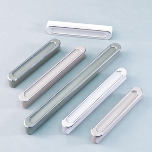 Puede incluir: Un conjunto de tiradores de armario modernos en varios tonos de plata y blanco. Cada tirador tiene forma rectangular con un centro ovalado empotrado. El herraje está diseñado para cajones y armarios.