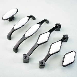 May include: A collection of black cabinet hardware, including a knob and several pulls. Each piece features a white oval or diamond-shaped center. The hardware is designed for furniture and cabinetry.