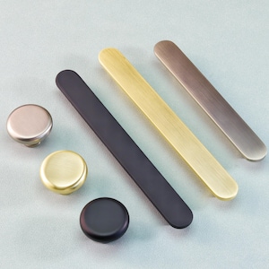 May include: A selection of cabinet hardware, including round knobs and rectangular bar pulls. The knobs are in silver, gold, and black finishes. The bar pulls are in black, gold, and bronze tones. All hardware is made of metal.