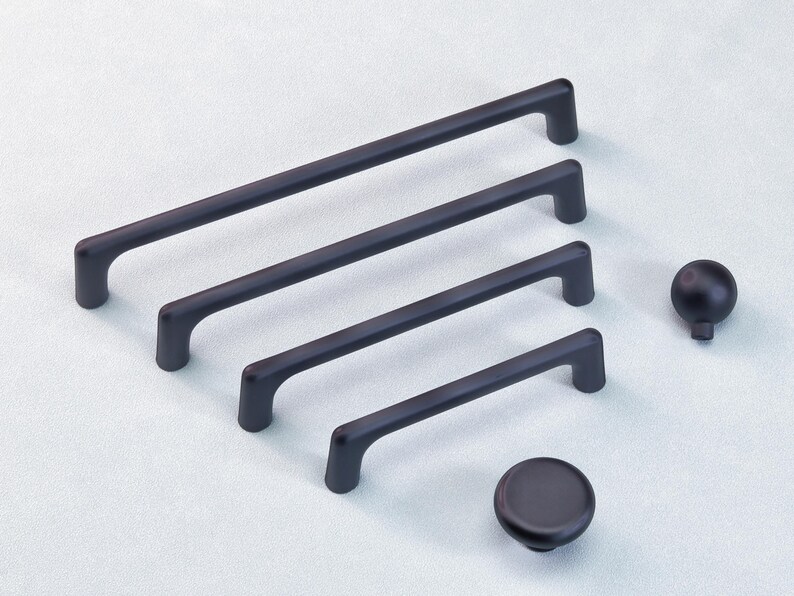 May include: A selection of black cabinet handles and knobs. There are four bar handles of varying lengths and two knobs, one spherical and one disc-shaped. The handles and knobs are all a matte black finish.