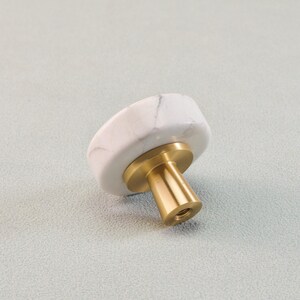 May include: A white marble cabinet knob with gray veining, mounted on a brass base. The knob has a rounded, irregular shape. The hardware is designed for furniture and home decor.