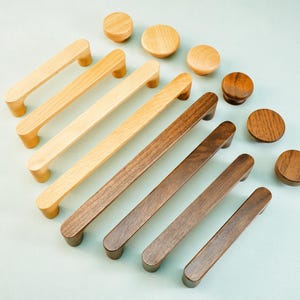 May include: A collection of wooden cabinet hardware, including handles and knobs, in various shades of brown. The handles are rectangular with rounded ends, and the knobs are circular. The hardware is arranged on a light blue surface.