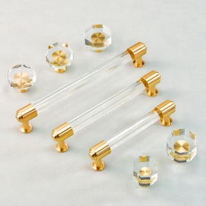 Puede incluir: Tiradores y pomos de armario de acrílico transparente con herrajes dorados. Los tiradores tienen un diseño cilíndrico, mientras que los pomos presentan tapas de cristal facetadas. Los herrajes son de color dorado brillante.
