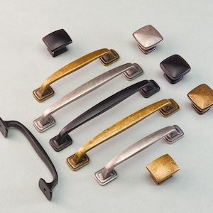 May include: A collection of cabinet hardware, including various pull handles and square knobs. The handles come in antique brass, silver, and black finishes. The knobs are in matching colors. The hardware is displayed on a light blue background.