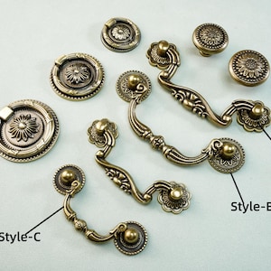 May include: An assortment of antique brass cabinet hardware, including knobs and pulls. Styles A, B, and C are labeled. The hardware features floral and ornate designs, suitable for furniture restoration or new builds.