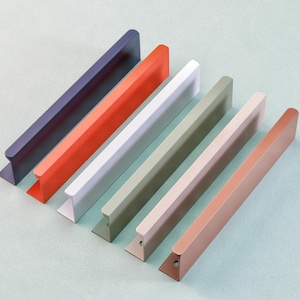 May include: Six colorful cabinet pulls in a row, each with a different color: navy, orange, white, olive green, beige, and copper. The pulls have a rectangular bar with a curved handle and a triangular base.