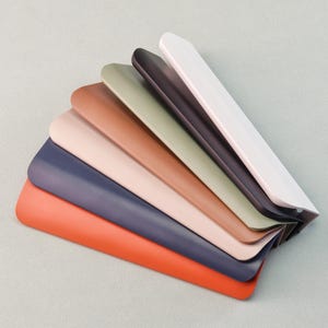 May include: A selection of shoe horns in various colours, including orange, navy, pink, brown, olive green, dark purple, and white. The shoe horns are fanned out, displaying their curved shape.