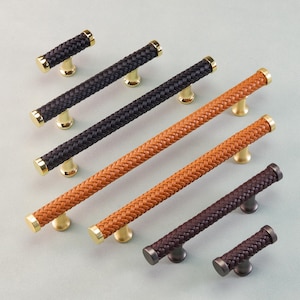 Op de afbeelding: Kastgrepen en knoppen in zwart, bruin en beige, met een geweven textuur en gouden of bronzen hardware. Deze decoratieve handgrepen zijn ontworpen voor meubels. Afmetingen in centimeters.