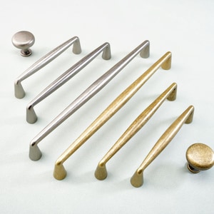 May include: A collection of cabinet hardware, including silver and gold-toned handles and knobs. The handles vary in size and shape, with a curved design. The knobs are round and have a matching finish. Ideal for kitchen or bathroom cabinets.
