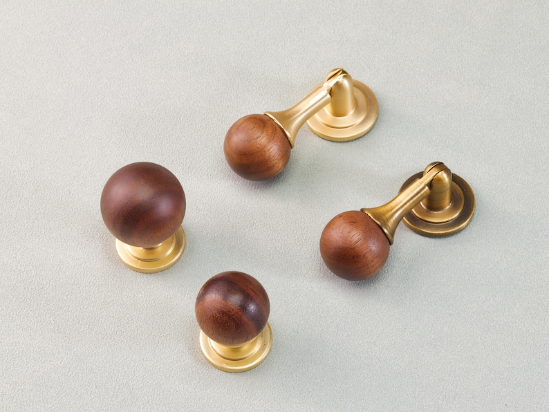 May include: Four pieces of hardware: two knobs and two pulls. The knobs have a round, dark brown wooden sphere atop a gold-colored base. The pulls have the same wooden sphere and gold base, with a curved arm.