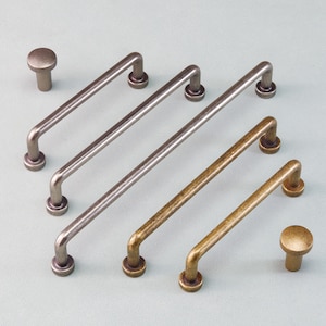 Puede incluir: Una colección de herrajes para gabinetes, que incluye dos perillas redondas y cuatro tiradores de barra en varios acabados metálicos. Los tiradores son rectos con extremos curvos, y los acabados incluyen plata, bronce y latón.