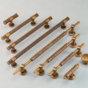 May include: Collection of bronze-toned cabinet hardware, including various sizes of bar pulls and knobs. The pulls have a textured, woven-like pattern, while the knobs feature a hammered design. Ideal for kitchen or bathroom renovations.