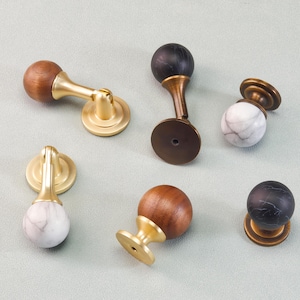 May include: A collection of cabinet knobs and pulls in various designs. Some feature a wooden sphere with a brass base, others have a marble sphere with a brass base, and some have a black marble sphere with a brass base.