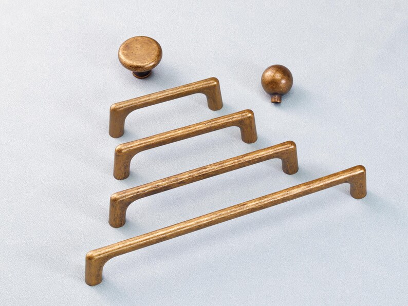 May include: A selection of antique brass cabinet hardware, comprising two knobs and three bar pulls. The knobs are round, and the pulls are rectangular with rounded ends. The hardware is presented against a light blue backdrop.