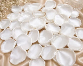 May include: A collection of numerous white artificial flower petals with a smooth, satin-like finish. Each petal features a rounded, slightly irregular shape with soft, curved edges, creating a layered and voluminous appearance in this display.