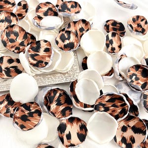May include: A collection of scattered artificial flower petals in two distinct styles. Some petals feature a brown, black, and tan leopard print pattern, while others are solid off-white. The petals have a smooth, rounded shape and a soft texture.