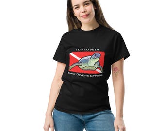 Puede incluir: Una camiseta negra de manga corta con un gráfico de una tortuga marina nadando sobre una bandera de buceo roja y blanca. El texto I DIVED WITH está impreso sobre la tortuga y EASY DIVERS CYPRUS está impreso debajo en letras blancas.