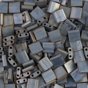 May include: A large pile of dark gray and silver square glass beads. The beads have two holes in each.
