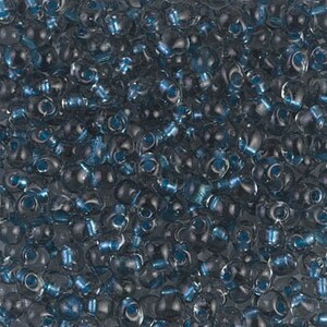 May include: A close-up image of a large quantity of small, round, iridescent blue glass beads. The beads have a slightly irregular shape and a metallic sheen.