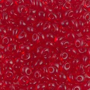 May include: A close-up of a large quantity of small, red, glass seed beads. The beads are opaque and have a slightly rounded, teardrop shape.