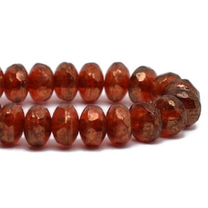 May include: Close-up of a strand of faceted, oval-shaped beads. The beads are a deep reddish-brown color with a metallic sheen. The beads are strung together, creating a necklace or bracelet.